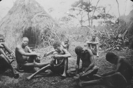 Gruppe afrikanischer Menschen vor einem Strohzelt sitzend.