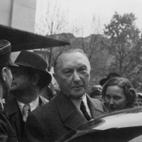 Adenauer vor einem Auto in die Kamera schauend