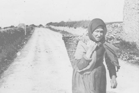 Frau mit Kopftuch und Korb auf dem Rücken.