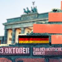 Symbolbild. Zertrümmerte Mauer mit Deutschlandflagge vor dem Brandenburgertor