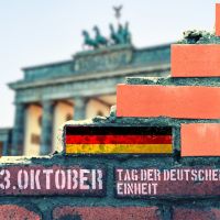 Symbolbild. Zertrümmerte Mauer mit Deutschlandflagge vor dem Brandenburgertor
