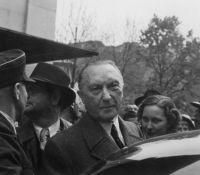 Adenauer vor Auto in die Kamera blickend.